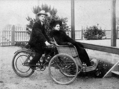 Woman in antique wheelchair on the front of a bicycle