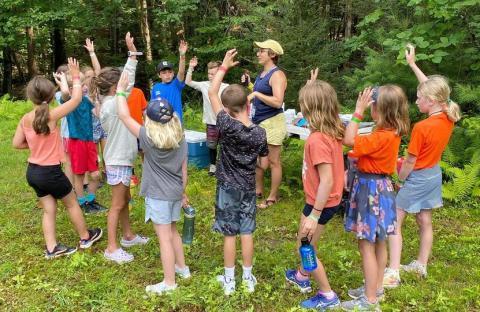 Kids in a circle at summer camp responding to a counselor.