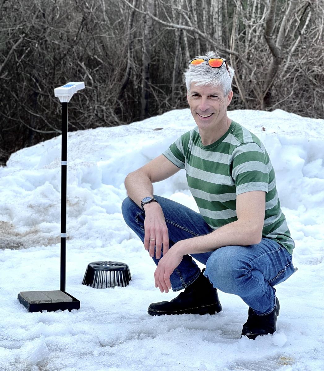 Man crouches in snow next to monitoring equipment