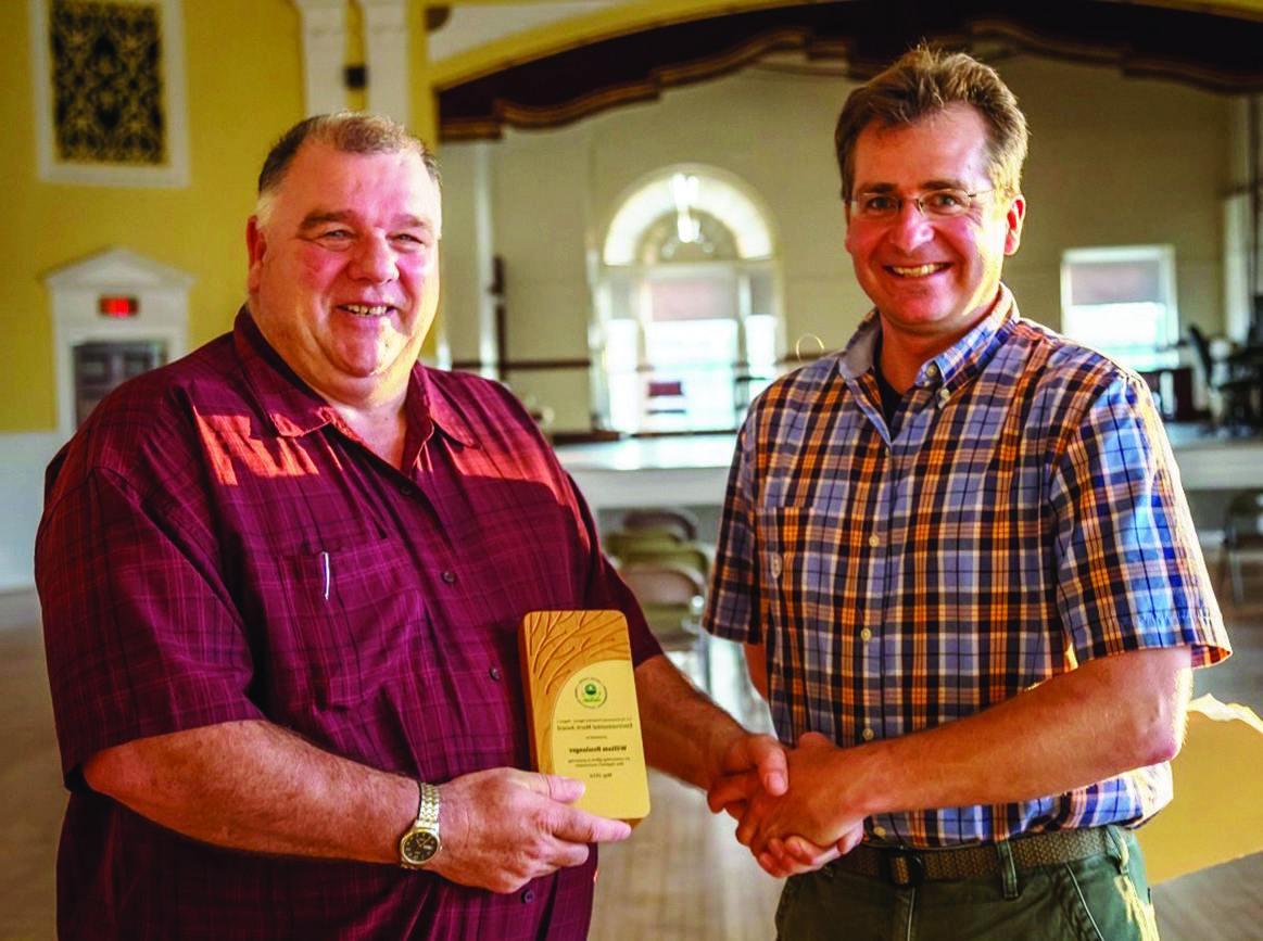 Jamie Houle and Bill Boulanger shake hands and hold a plaque