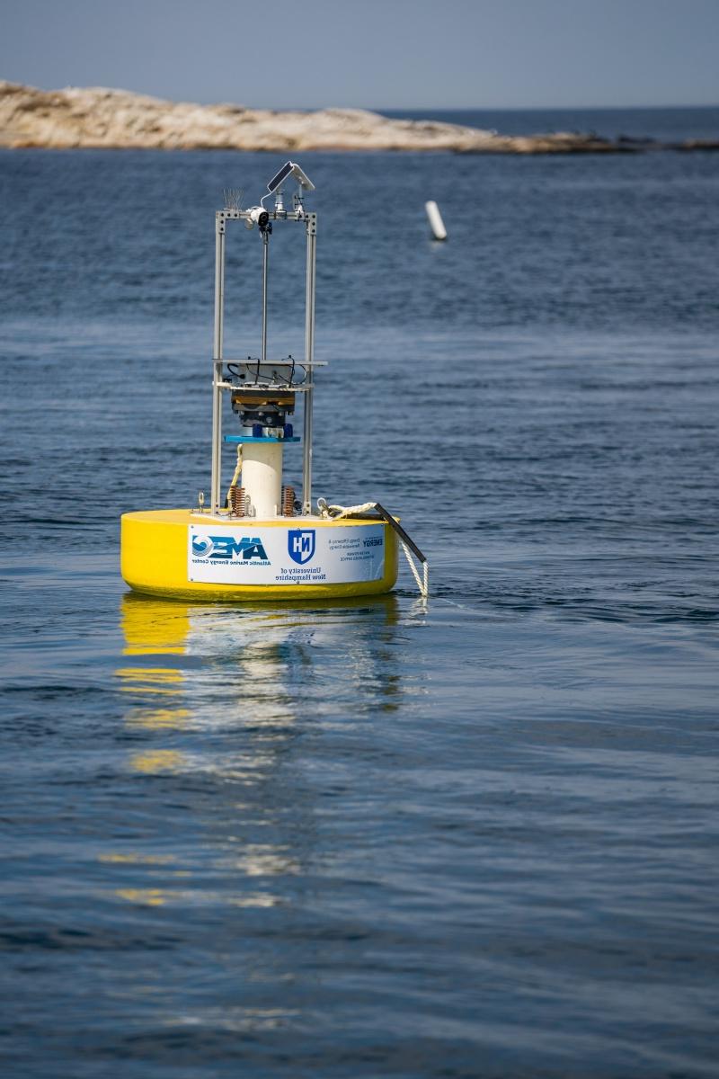 Yellow University of New Hampshire marine energy buoy at sea, with island in background