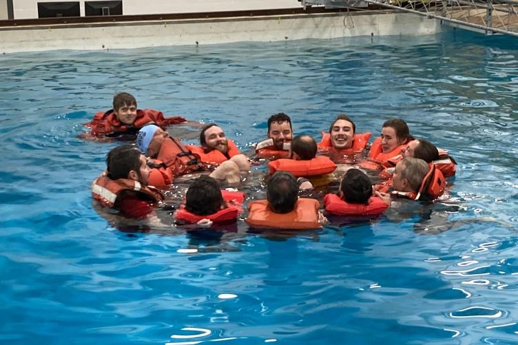 Group of people wearing lifejackets huddle in a circle in a pool