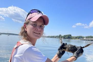 Female graduate student on a boat holding a male blue crab