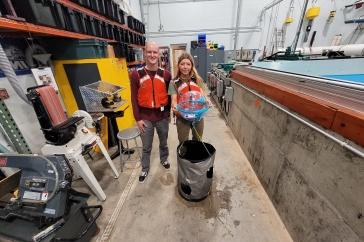 Two 主要研究 student 研究ers hold their winning ocean renewable energy device in front of a wave tank. 他们穿着红色的救生衣.