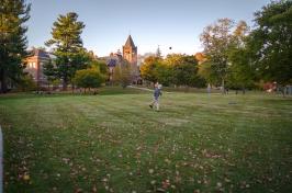 Student walking across lawn, T Hall in the background 