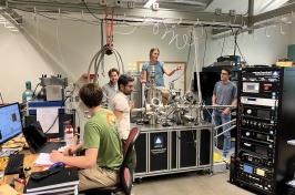 Five people work in a lab full of computers 和 other equipment