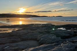 A scenic photo of the Gulf of 缅因州 shoreline showing two people walking into a sunset.