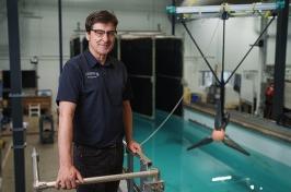 Male researcher stands above engineering test tank with large turbine behind