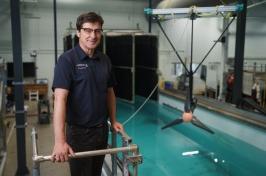 Male researcher stands above engineering test tank with large turbine behind