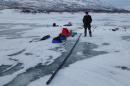 Young man dressed in warm winter clothing stands on frozen lake next to long series of black sediment cores. 