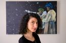 Woman with dark curly hair looks at the camera, painting of Black astronomers behind her