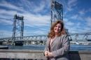 Woman with brown hair wearing gray suit stands in front of Memorial Bridge in Portsmouth.