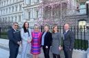 Six people in business attire standing for a photo outside the Eisenhower Executive Office Building in Washington, DC. 他们后面是一棵盛开的樱桃树.